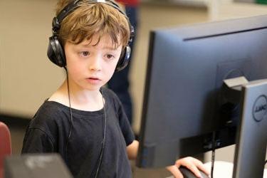 一个年轻的学生戴着耳机坐在电脑前